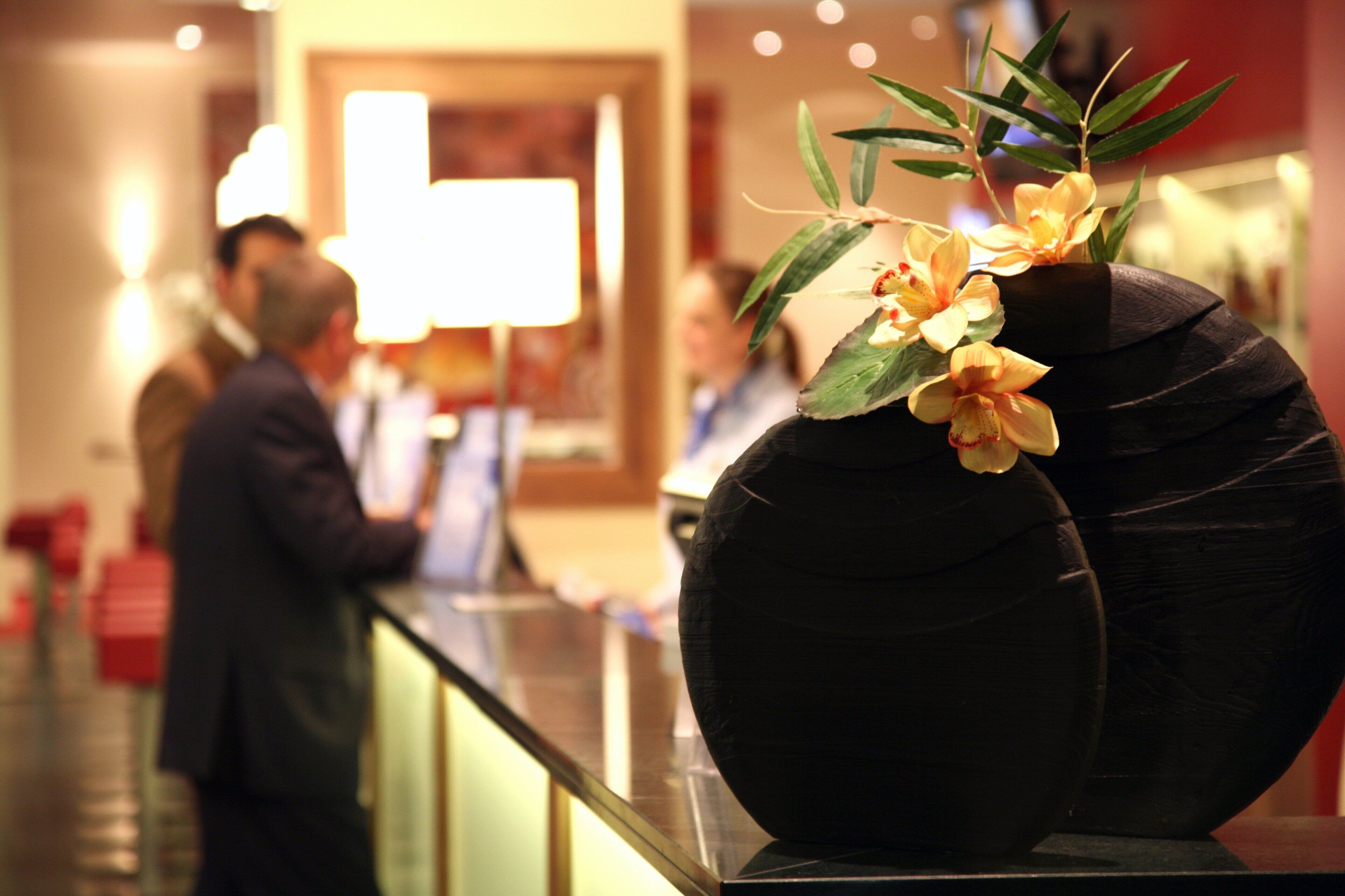 Eine Vase mit Blumen auf einer spiegelnden Fläche in einem öffentlichen Innenraum.