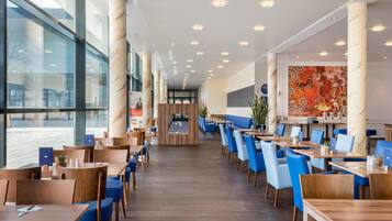 A modern restaurant with a long counter, blue chairs, and a large window.