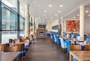 A modern restaurant with a long counter, blue chairs, and a large window. - Holiday Inn Express Singen by IHG (Singen)