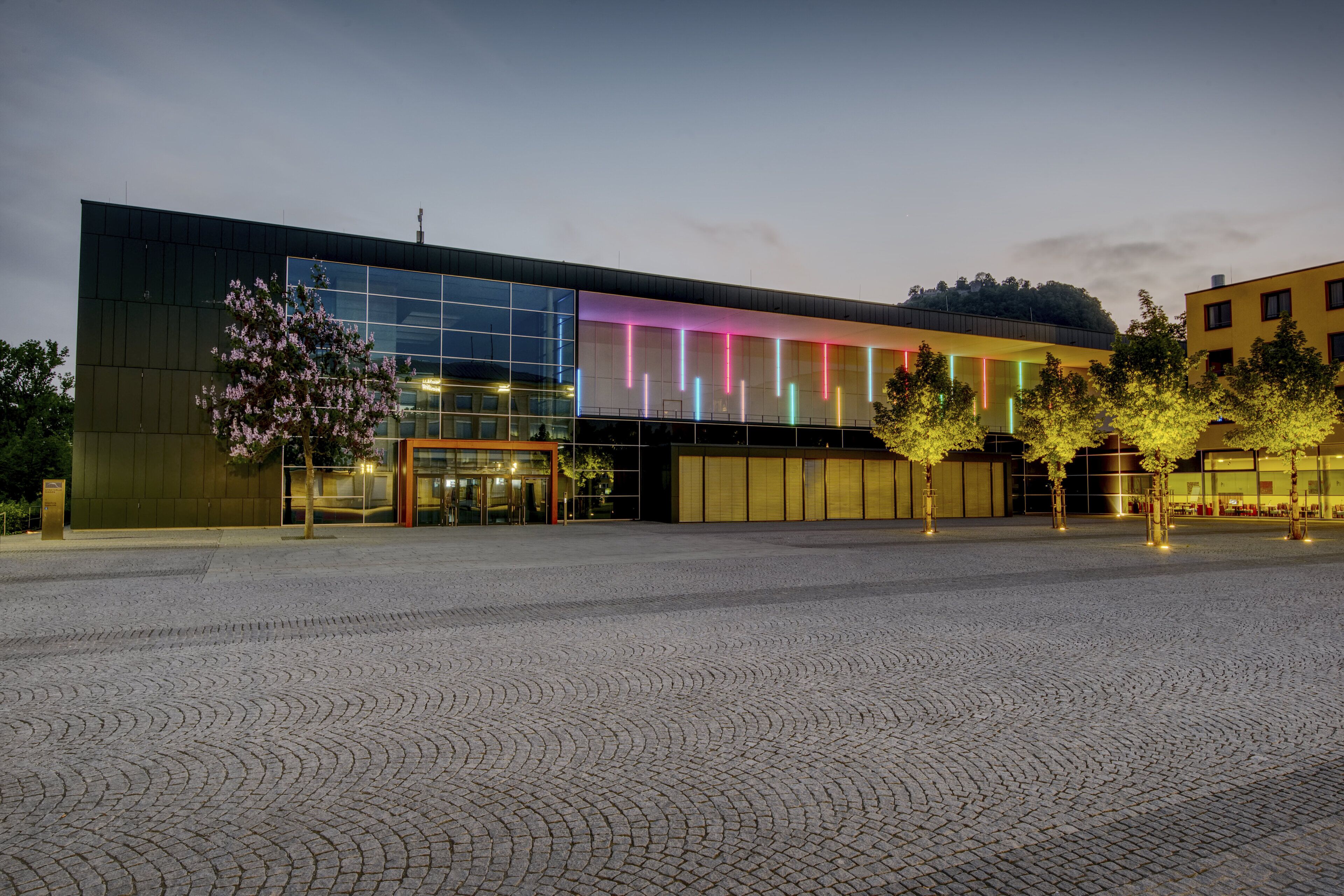 A modern building with a glass facade and a paved courtyard.