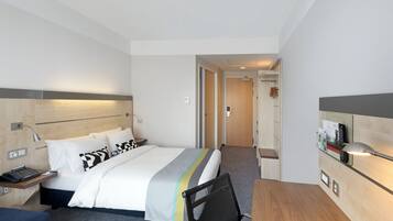 Quarto de hotel com cama, mesa de cabeceira, abajur e escrivaninha com cadeira.