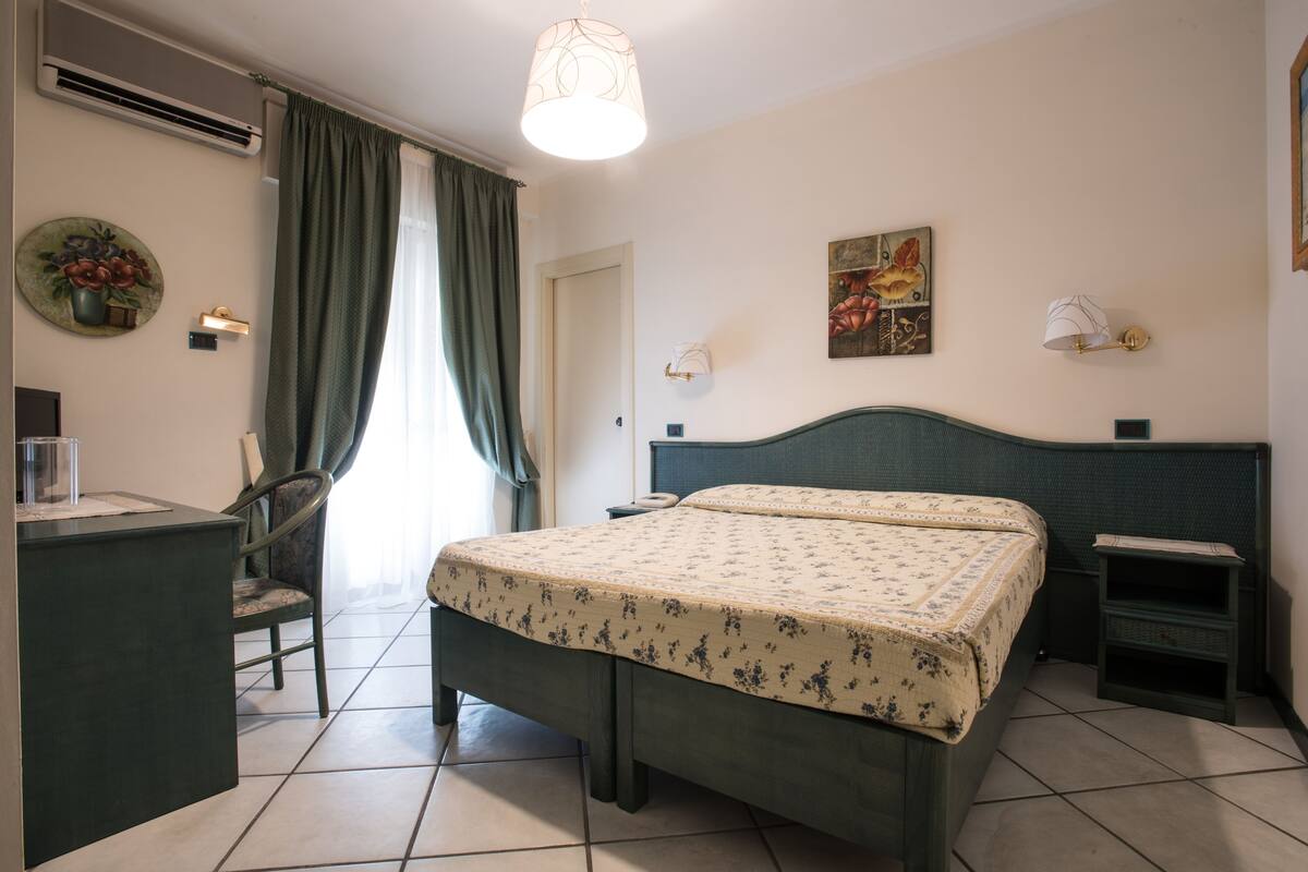A bedroom with a bed, a desk, a chair, a lamp, and a wall-mounted artwork.