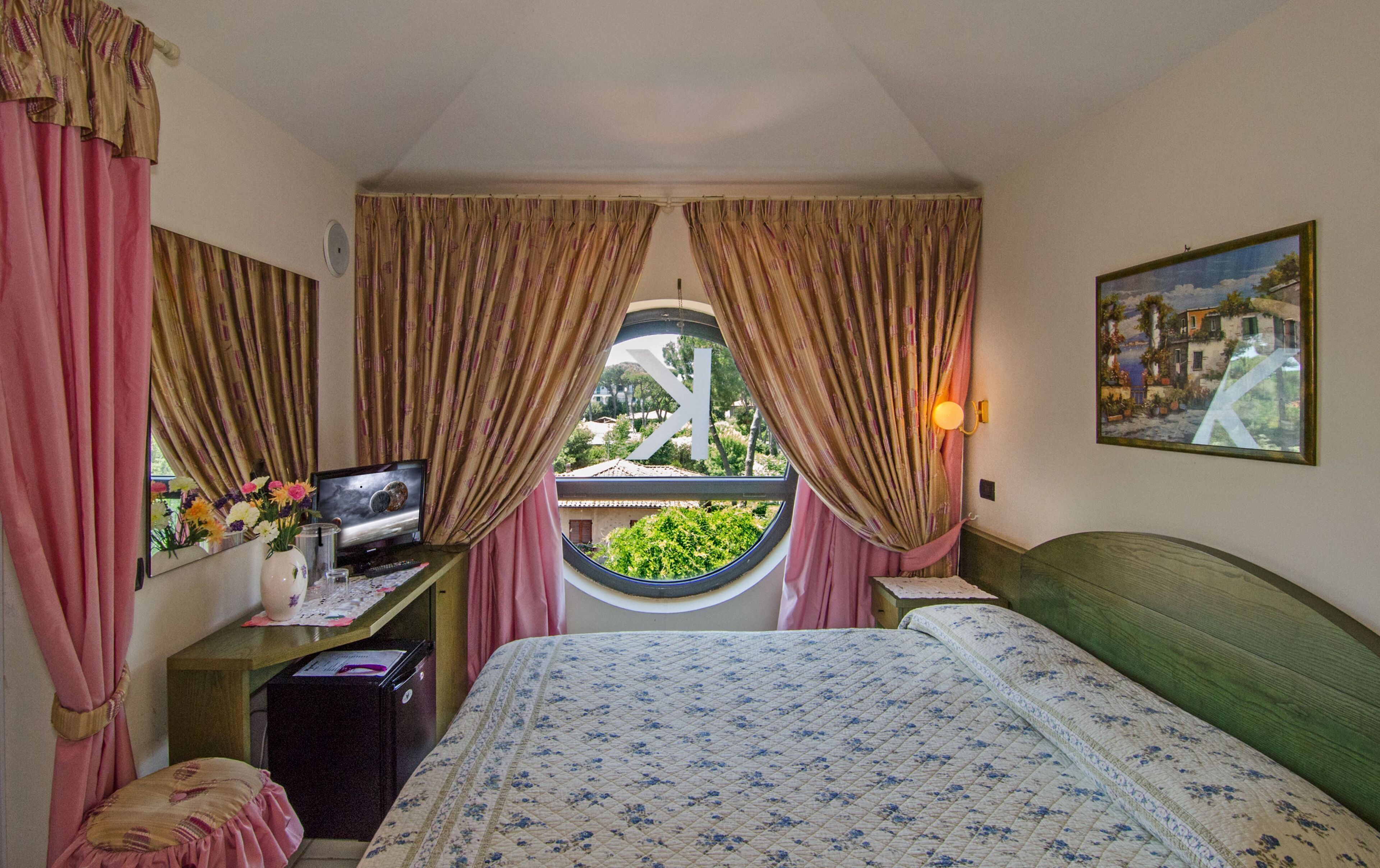 Una camera da letto con un letto, una scrivania con un computer, una finestra con tende e un quadro appeso al muro.
