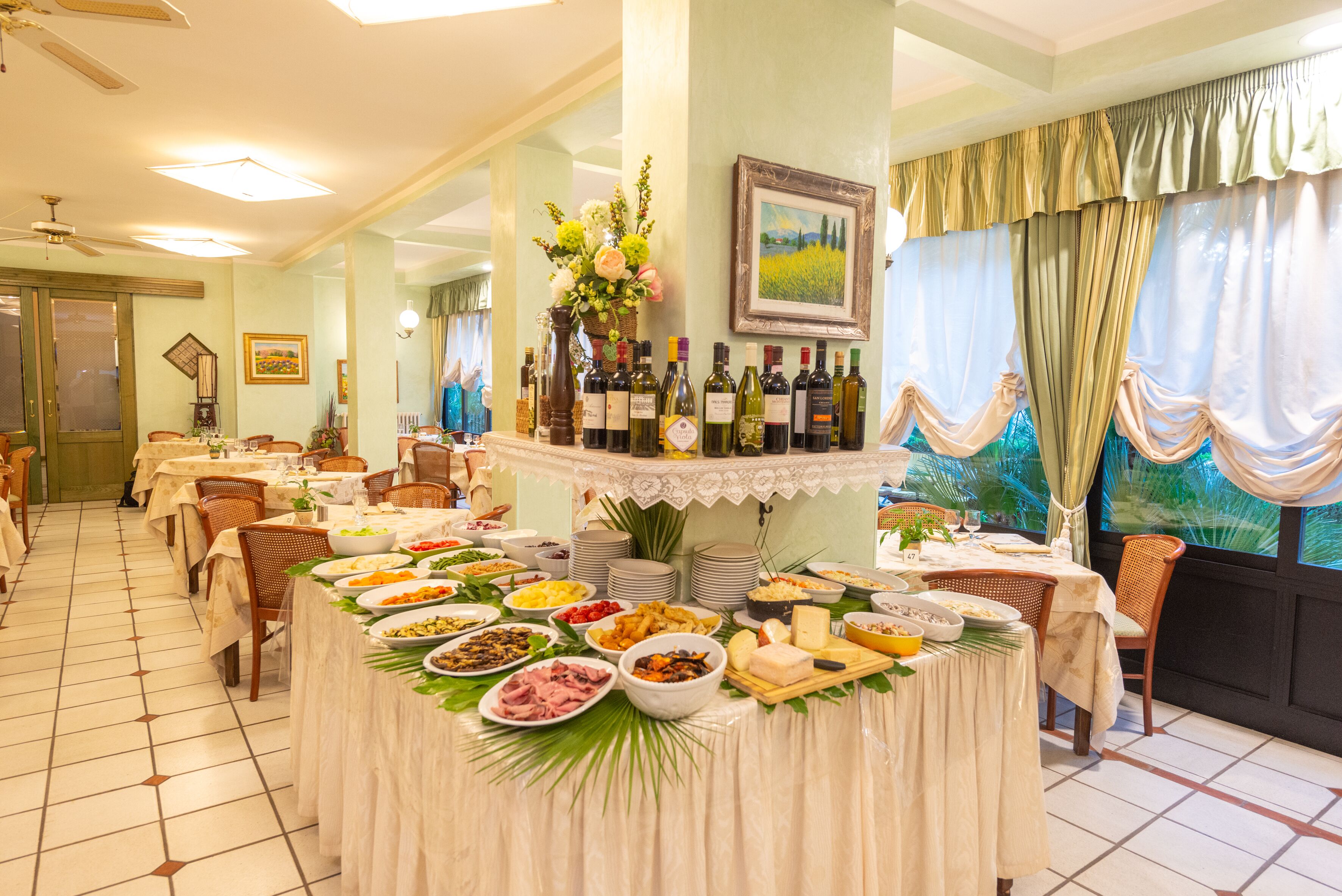A dining area with multiple tables, a buffet with various food items, and a selection of wine bottles.