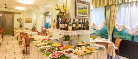 A dining area with multiple tables, a buffet with various food items, and a selection of wine bottles.