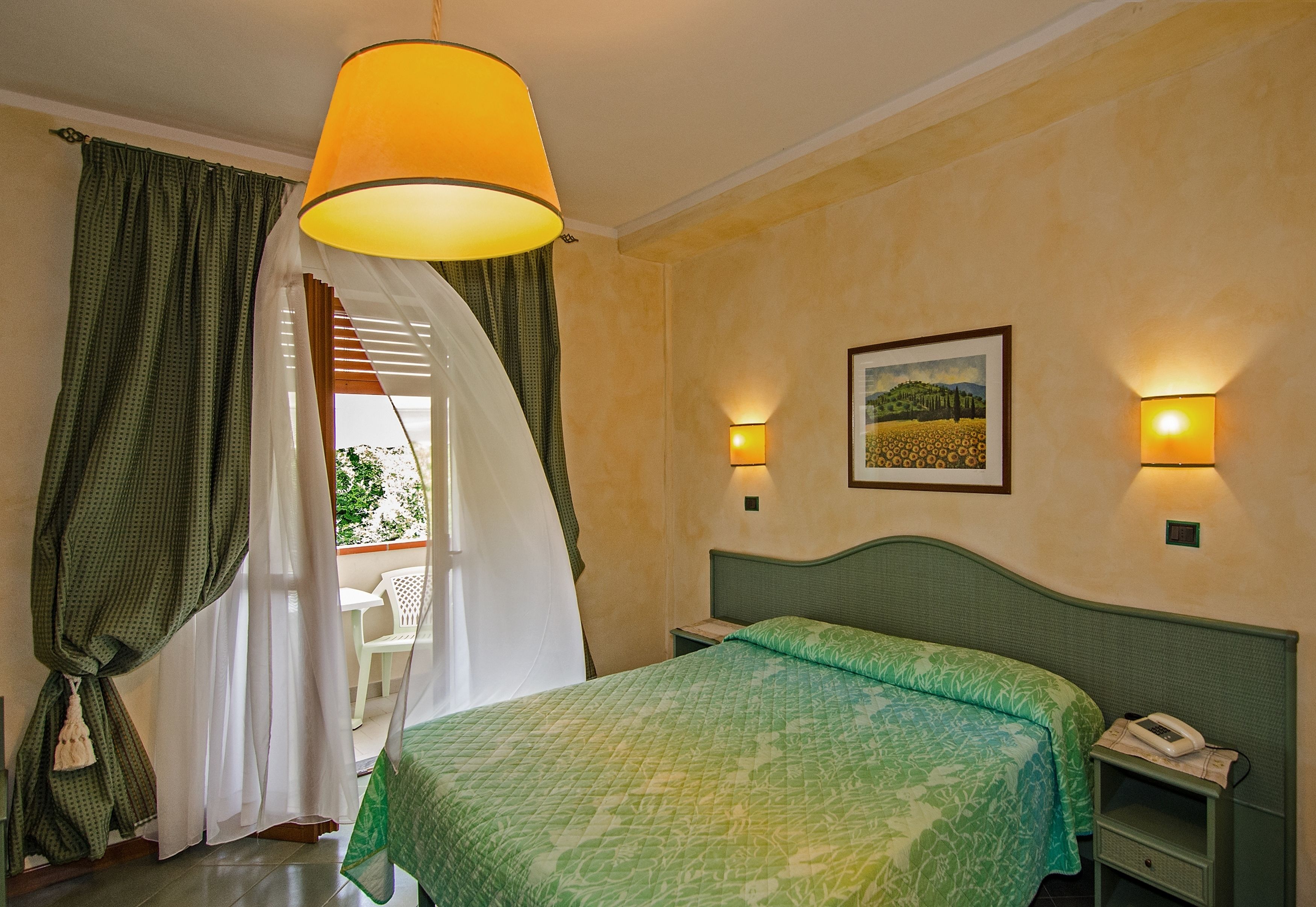 Habitación de hotel con cama, mesita de noche con teléfono, lámpara de pared e imagen en la pared.