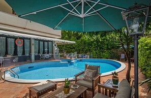 A swimming pool with a sunshade, lounge chairs, and a table with a plant. - Hotel Kyrton (Forte dei Marmi)