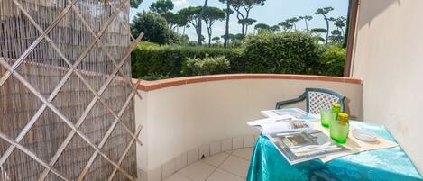 Un balcon avec une table dressée pour deux personnes, un paravent en osier et une vue sur les arbres.