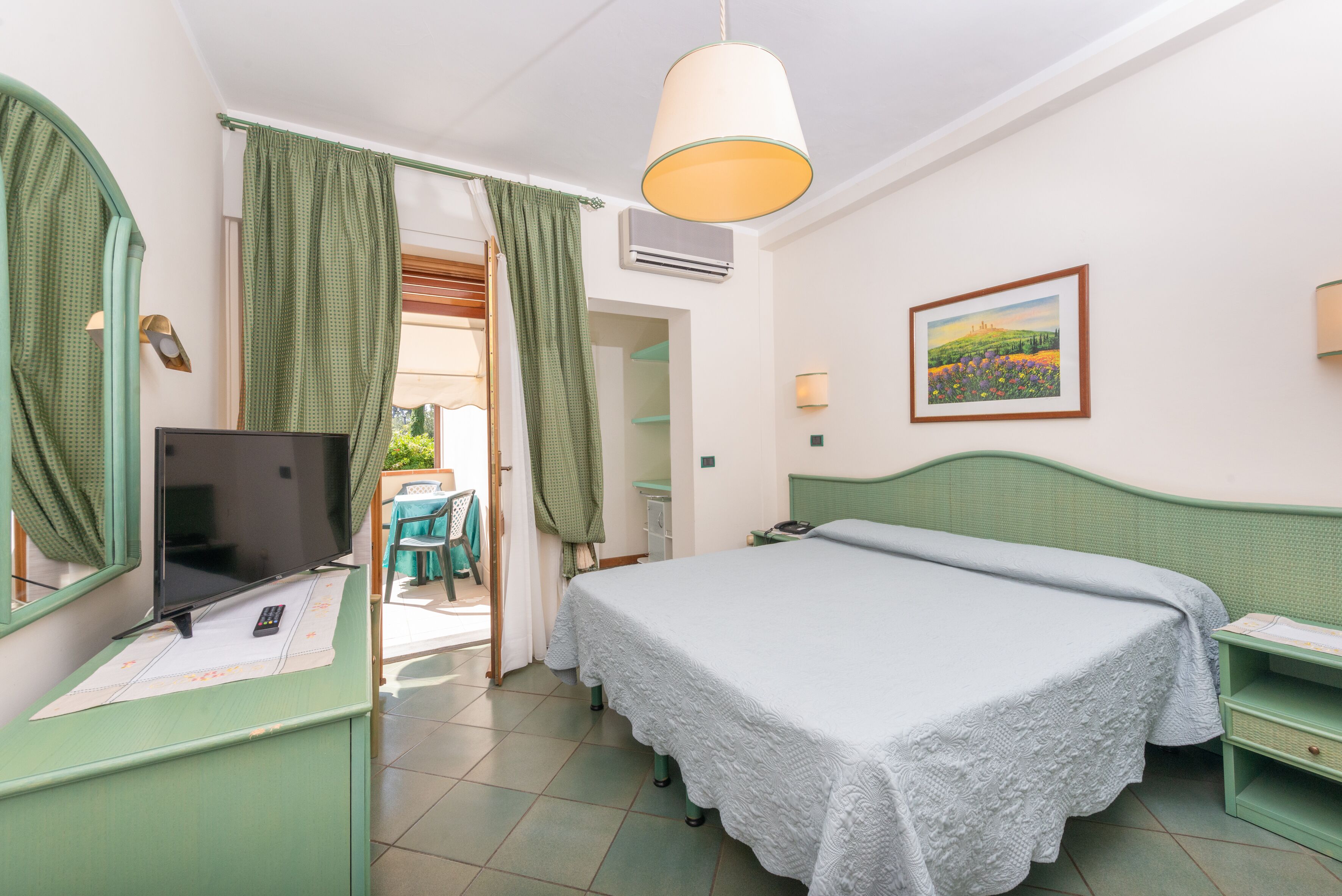 Une chambre à coucher avec un lit, un bureau avec une télévision, une chaise et un tableau accroché au mur.