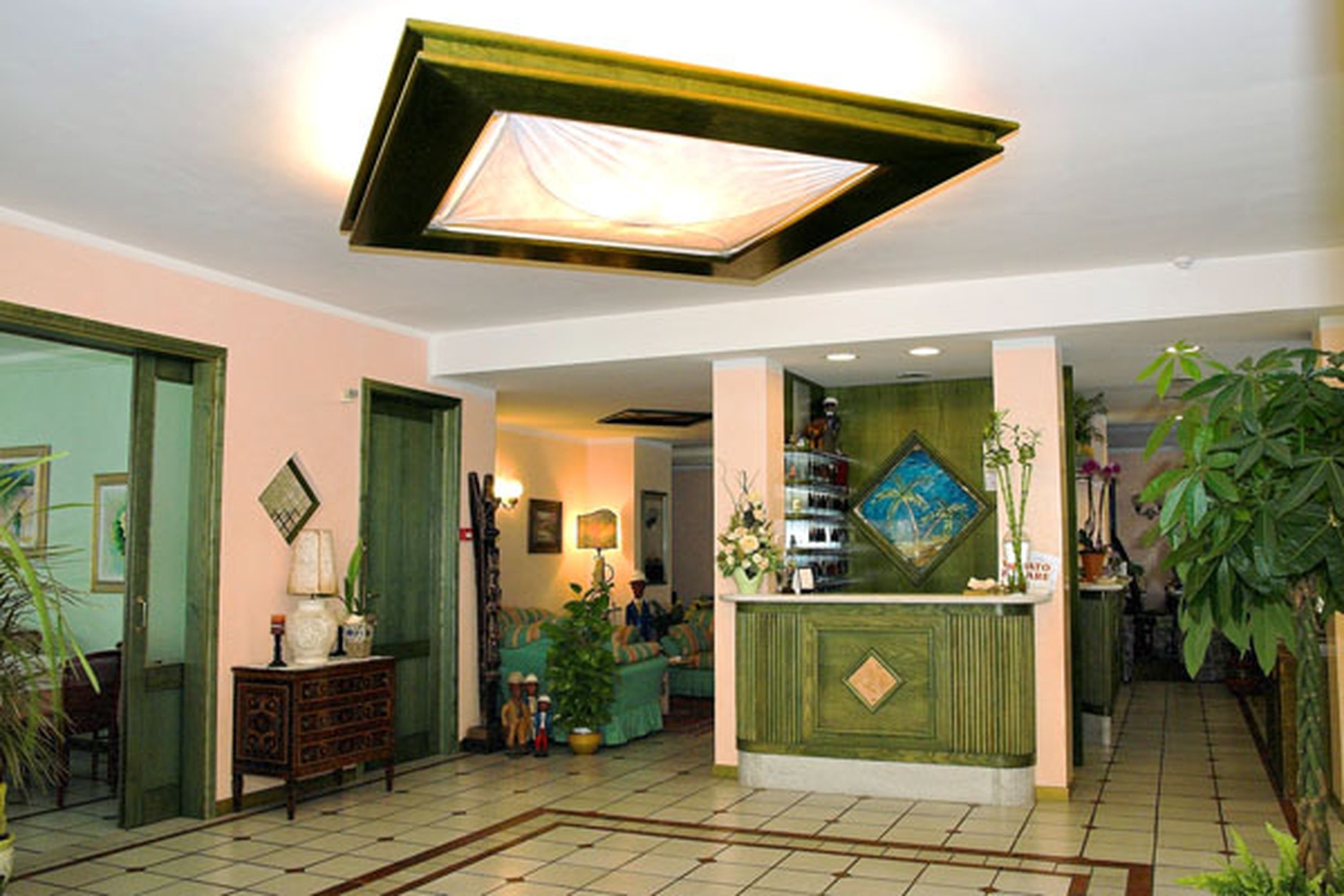 A lobby with a reception desk, a green wall with a painting, and a tiled floor.