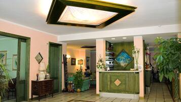 A lobby with a reception desk, a green wall with a painting, and a tiled floor.