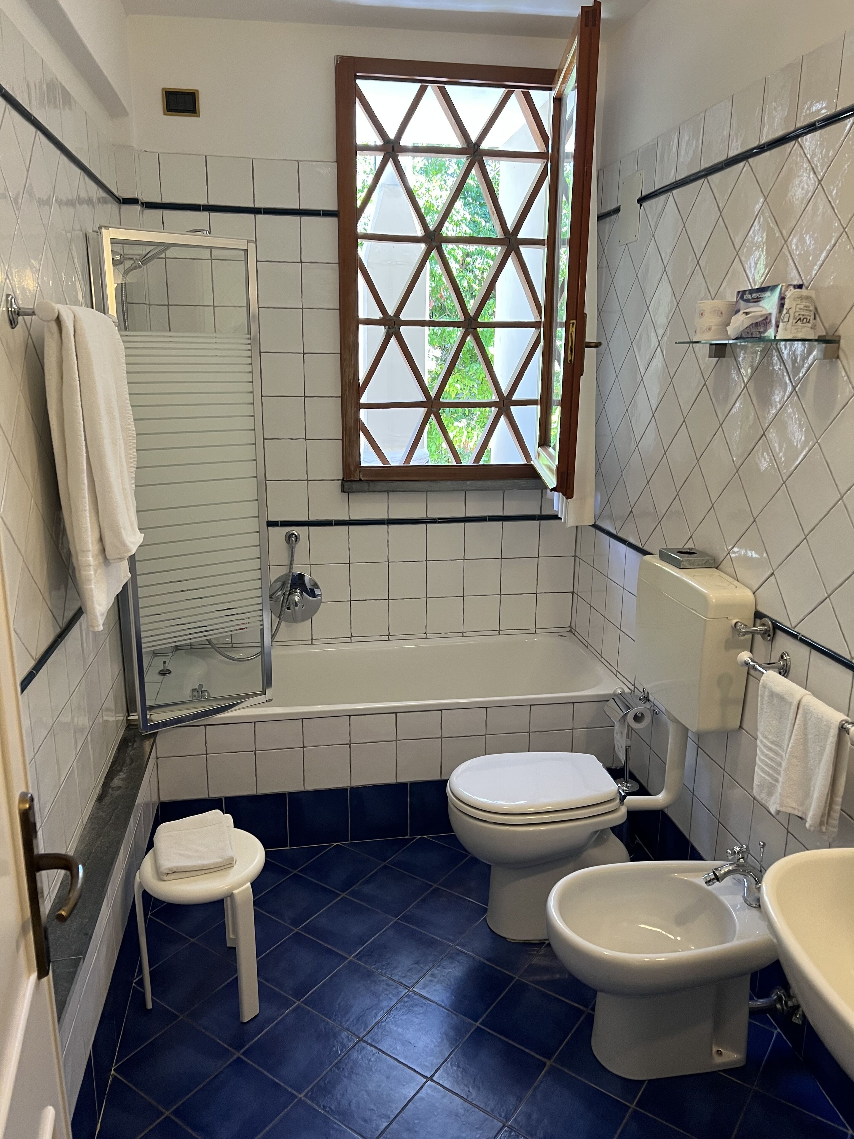 Un baño con bañera, inodoro, bidé y una ventana con diseño de celosía.