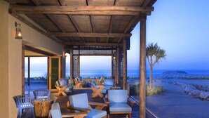 Une terrasse en bois avec des sièges extérieurs, une vue sur l’océan et un espace abrité agrémenté d’une structure en treillis.
