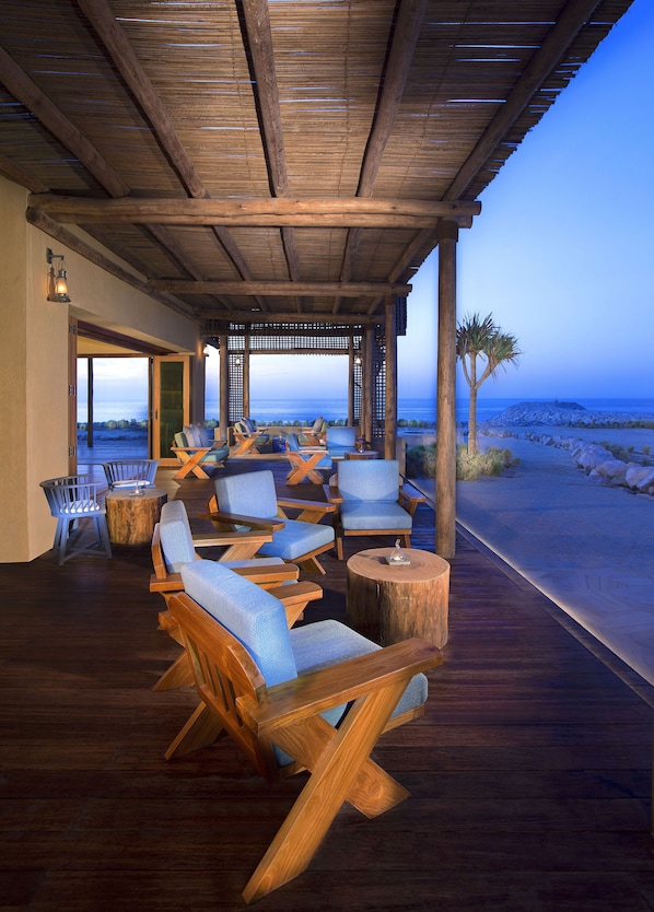 A wooden deck with outdoor seating, a view of the ocean, and a covered area with a lattice design.
