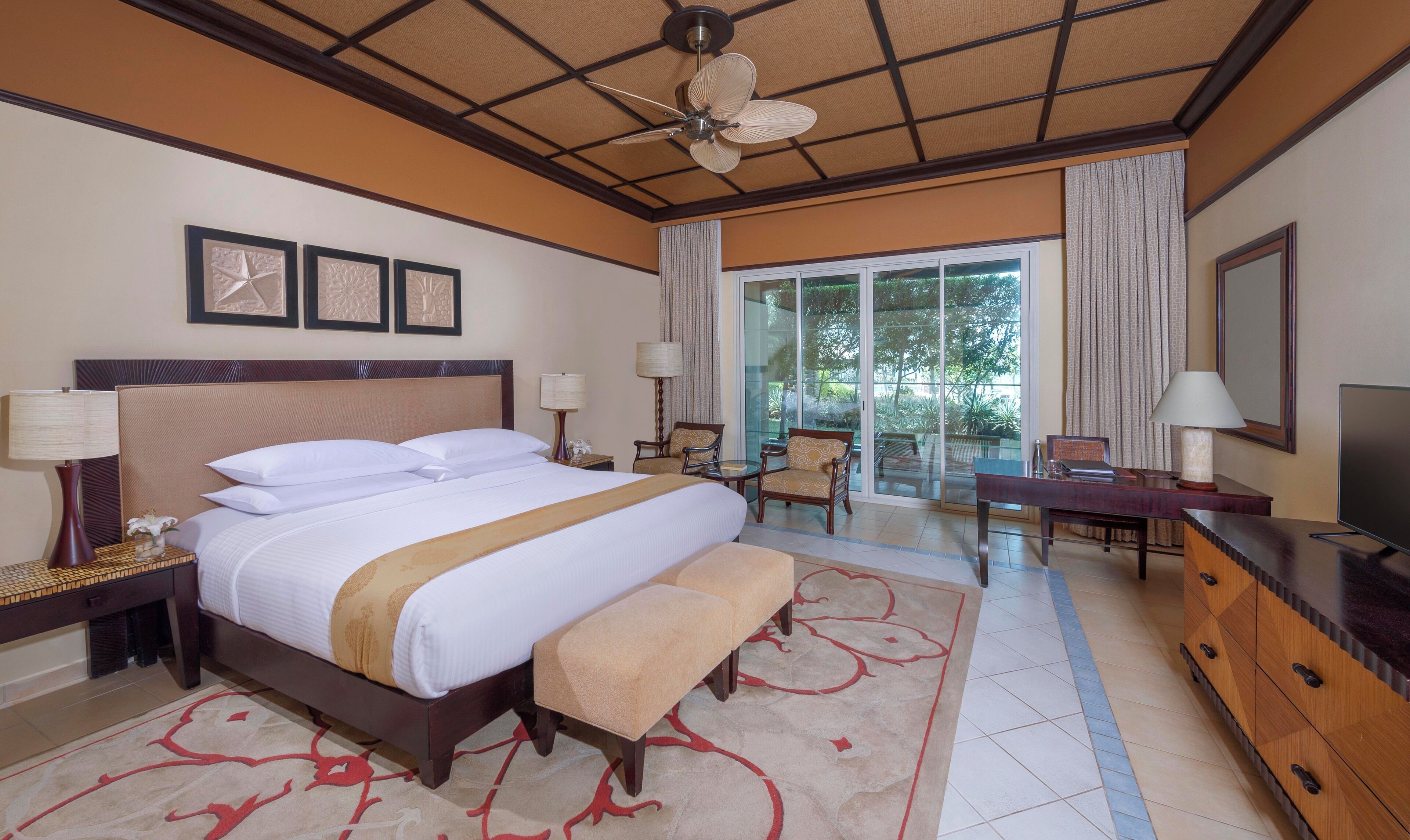 Une chambre d’hôtel avec un grand lit, un bureau, une télévision et un balcon donnant sur la verdure.