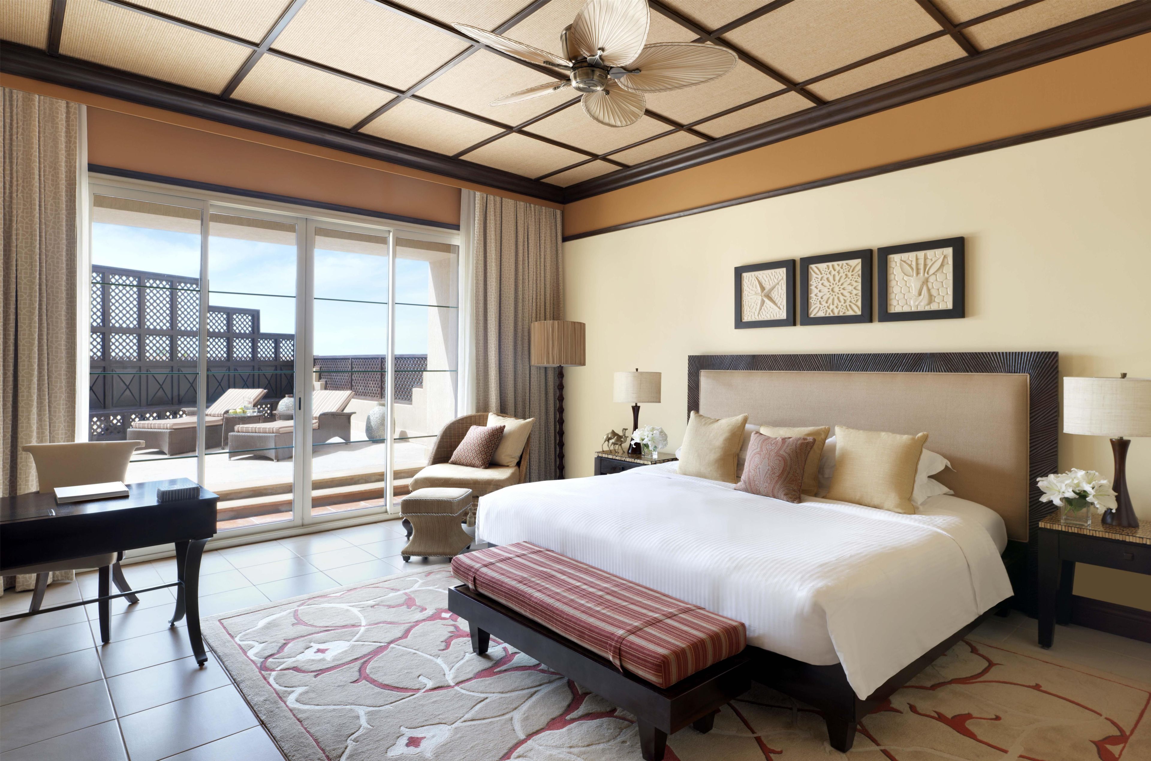 A hotel room with a large bed, a desk, a chair, and a balcony with outdoor furniture.