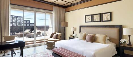 A hotel room with a large bed, a desk, a chair, and a balcony with outdoor furniture.