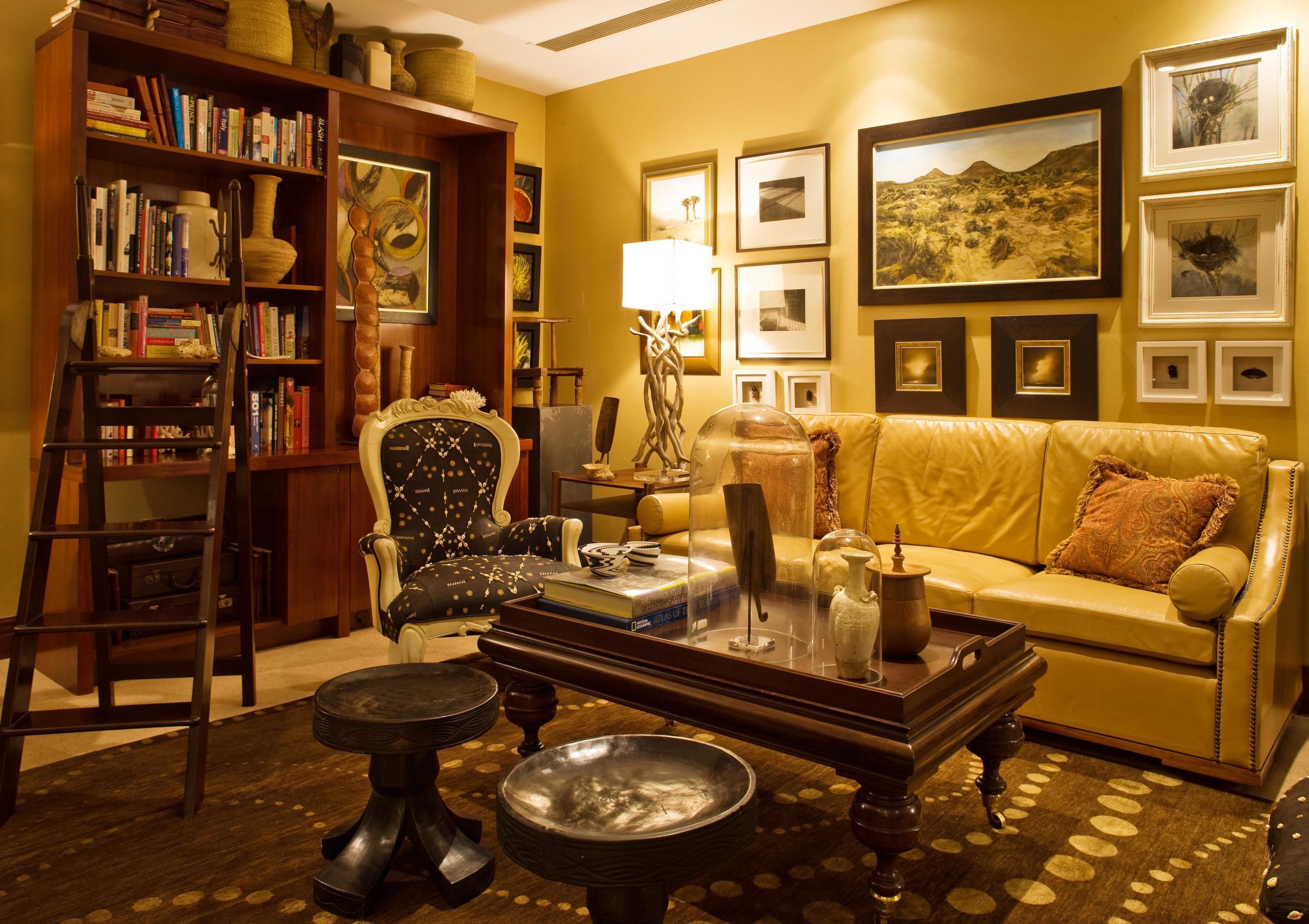 A cozy living room with a yellow sofa, a wooden coffee table, a bookshelf, and framed artwork on the walls.