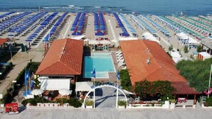 Um hotel à beira-mar com piscina, vários guarda-sóis de praia e uma vista desobstruída do oceano.