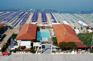Un hotel frente a la playa con piscina, varias sombrillas y vista despejada al océano.