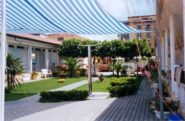 Un pati amb una tenda estriada, plantes en testos i un camí.