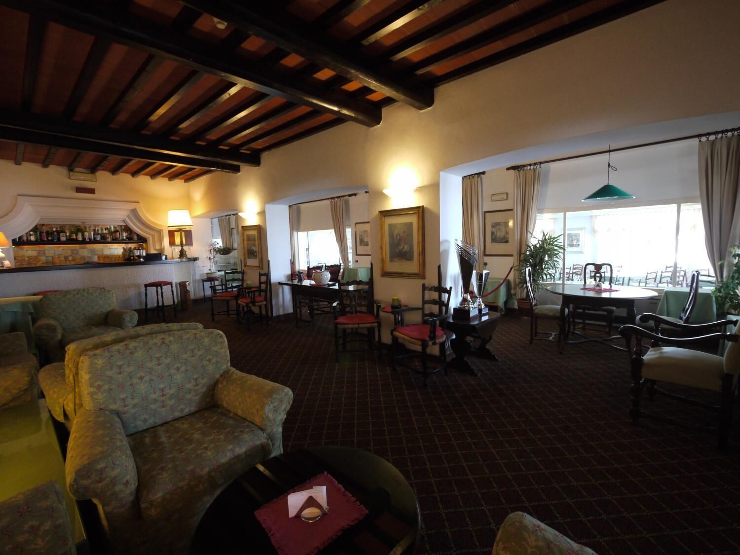 A spacious hotel lobby with a bar area, multiple seating arrangements, and large windows providing natural light.