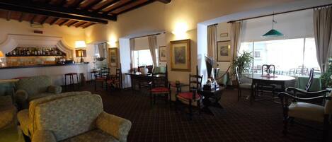 A spacious hotel lobby with a bar area, multiple seating arrangements, and large windows providing natural light.