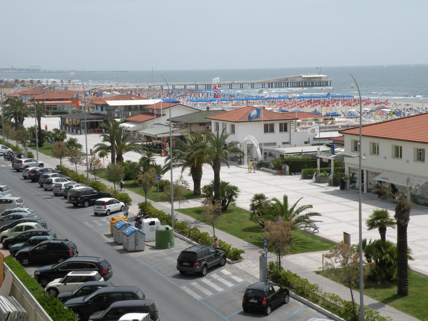 A coastal hotel with a parking lot, beach view, and a pier in the background.