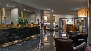 A modern hotel lobby with a marble reception desk, leather seating, and a well-lit interior.