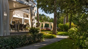 A modern building with a covered outdoor seating area, a garden pathway, and lush greenery.