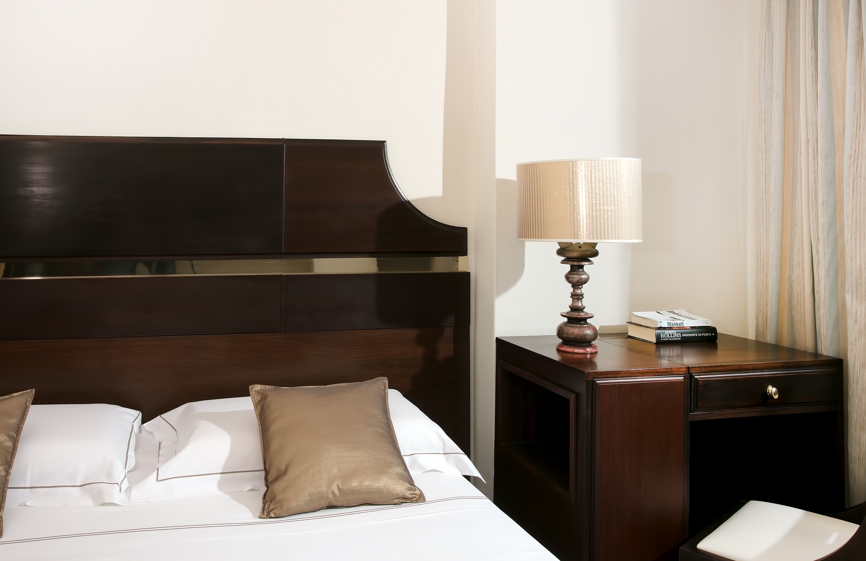 A hotel room with a large bed, a wooden nightstand with a lamp, and a small desk with a telephone.