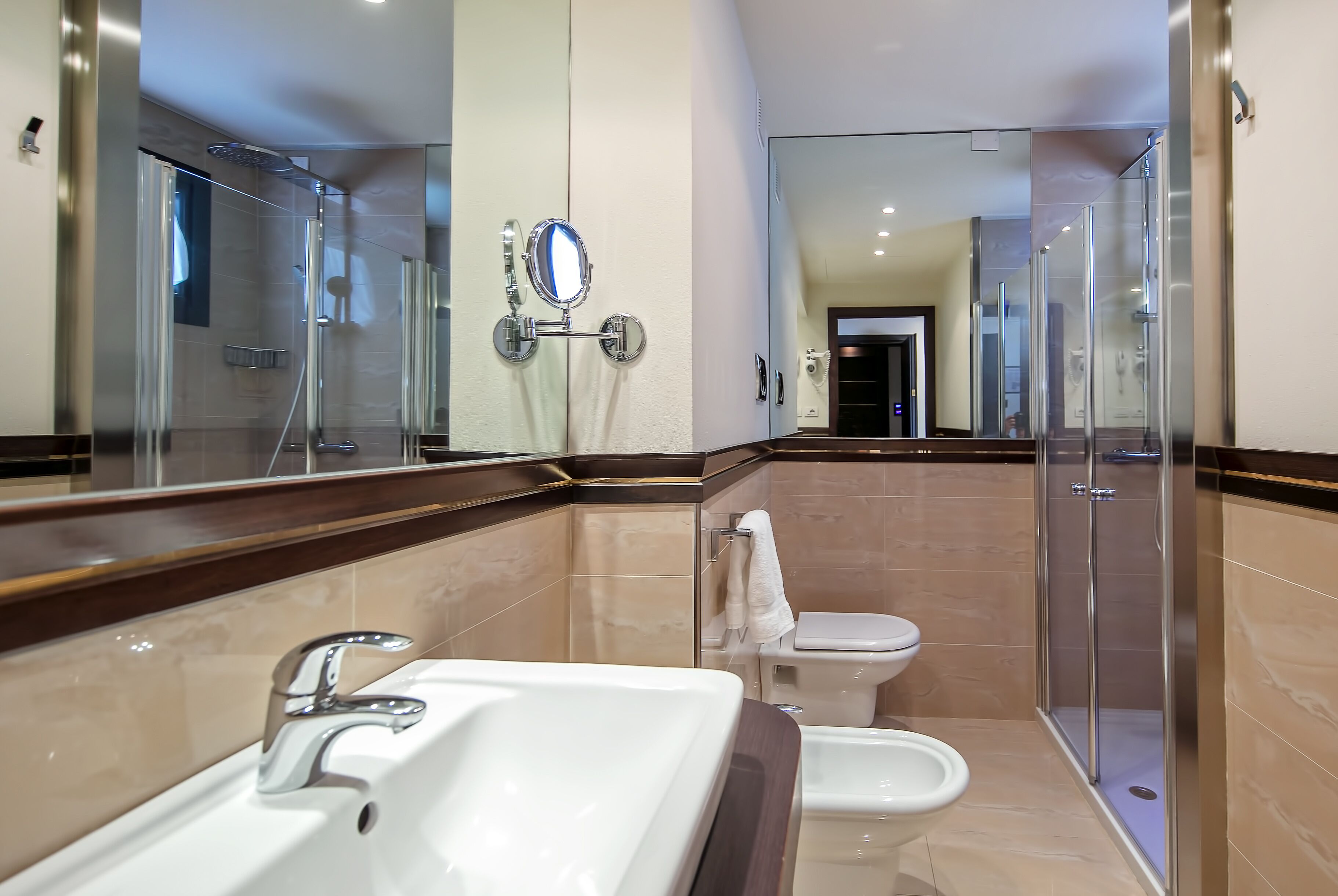A modern bathroom with a large mirror, a sink, a bidet, and a glass-enclosed shower.