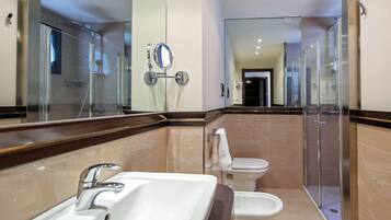A modern bathroom with a large mirror, a sink, a bidet, and a glass-enclosed shower.