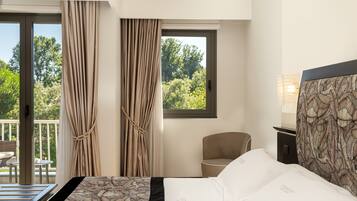 A hotel room with a bed, a chair, a desk, and a view of greenery outside.