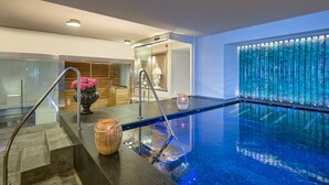 A modern indoor pool with clear glass walls, a wooden floor, and a staircase leading to the pool area.