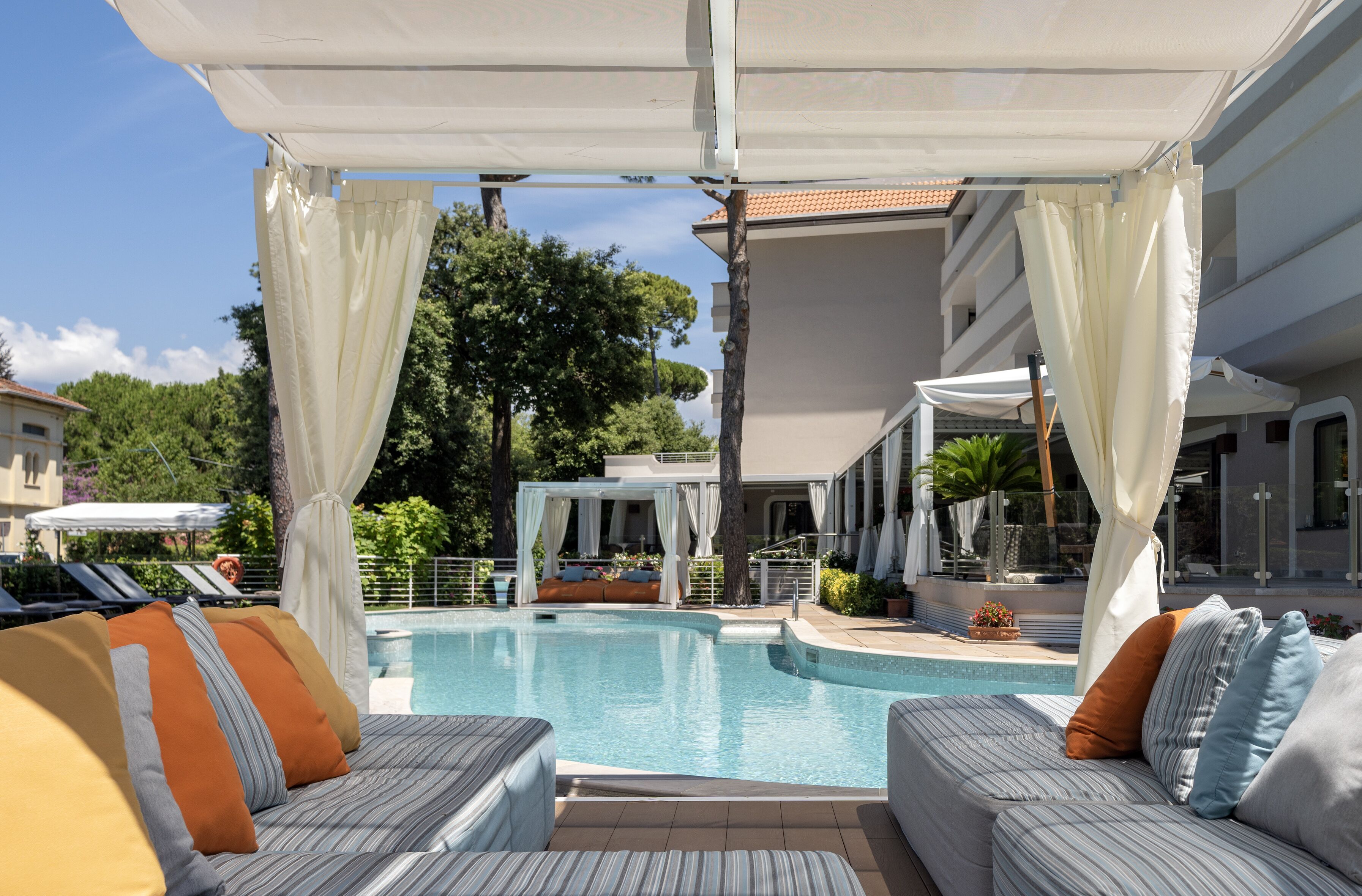 A poolside area with a covered seating area, a pool, and a view of the surrounding landscape.