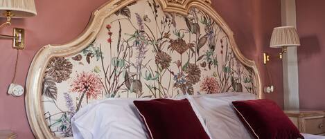A bed with white linens and two red pillows, a floral headboard, and two bedside lamps.