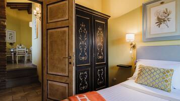 Una camera d'albergo con un letto, un comodino, una lampada, un quadro floreale incorniciato e un armadio in legno.