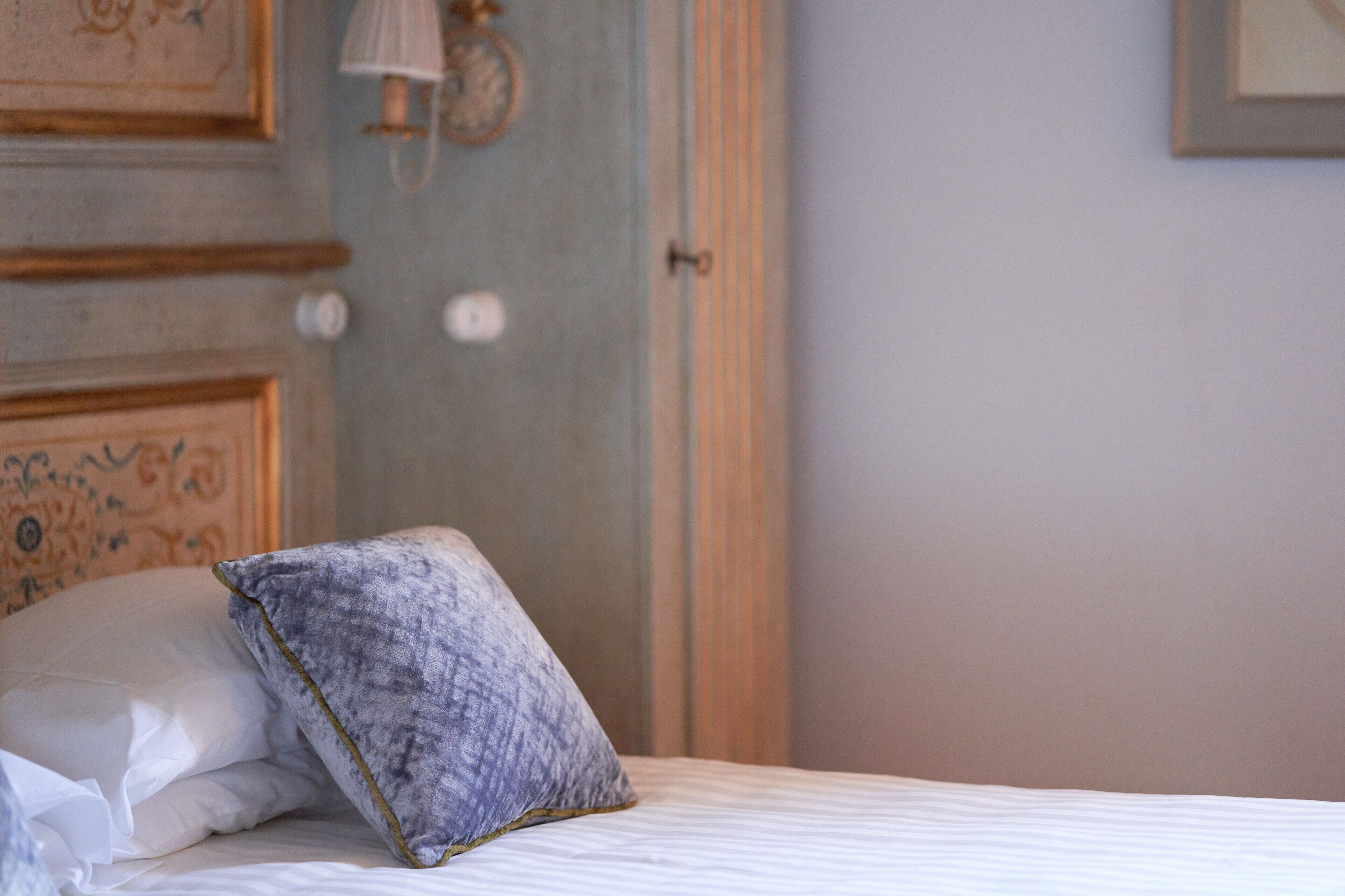 Una cama con ropa de cama blanca y una almohada gris, un reloj de pared y una puerta con marco de madera.