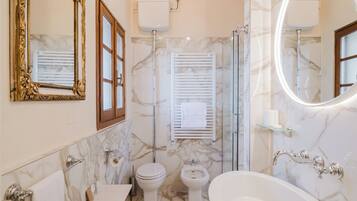 A bathroom with a toilet, bidet, bathtub, and a large mirror.