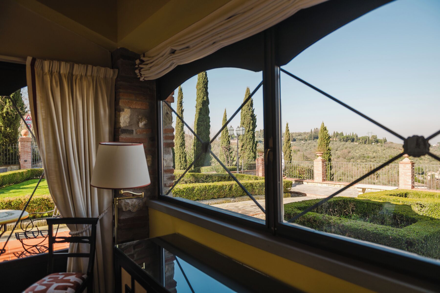 Una habitación con vistas a un jardín ajardinado, una lámpara y una silla.