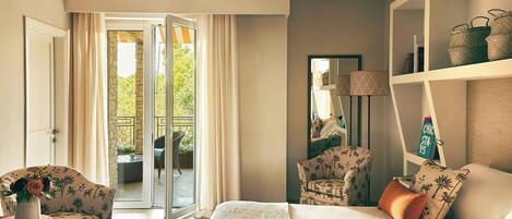 Habitación de hotel con cama, una silla, un escritorio, una estantería y un ventanal corredero que da a un espacio exterior.