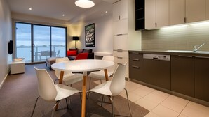 Una cocina moderna con lavavajillas, una zona de comedor con una mesa redonda y sillas blancas, y un ventanal con vistas al agua.