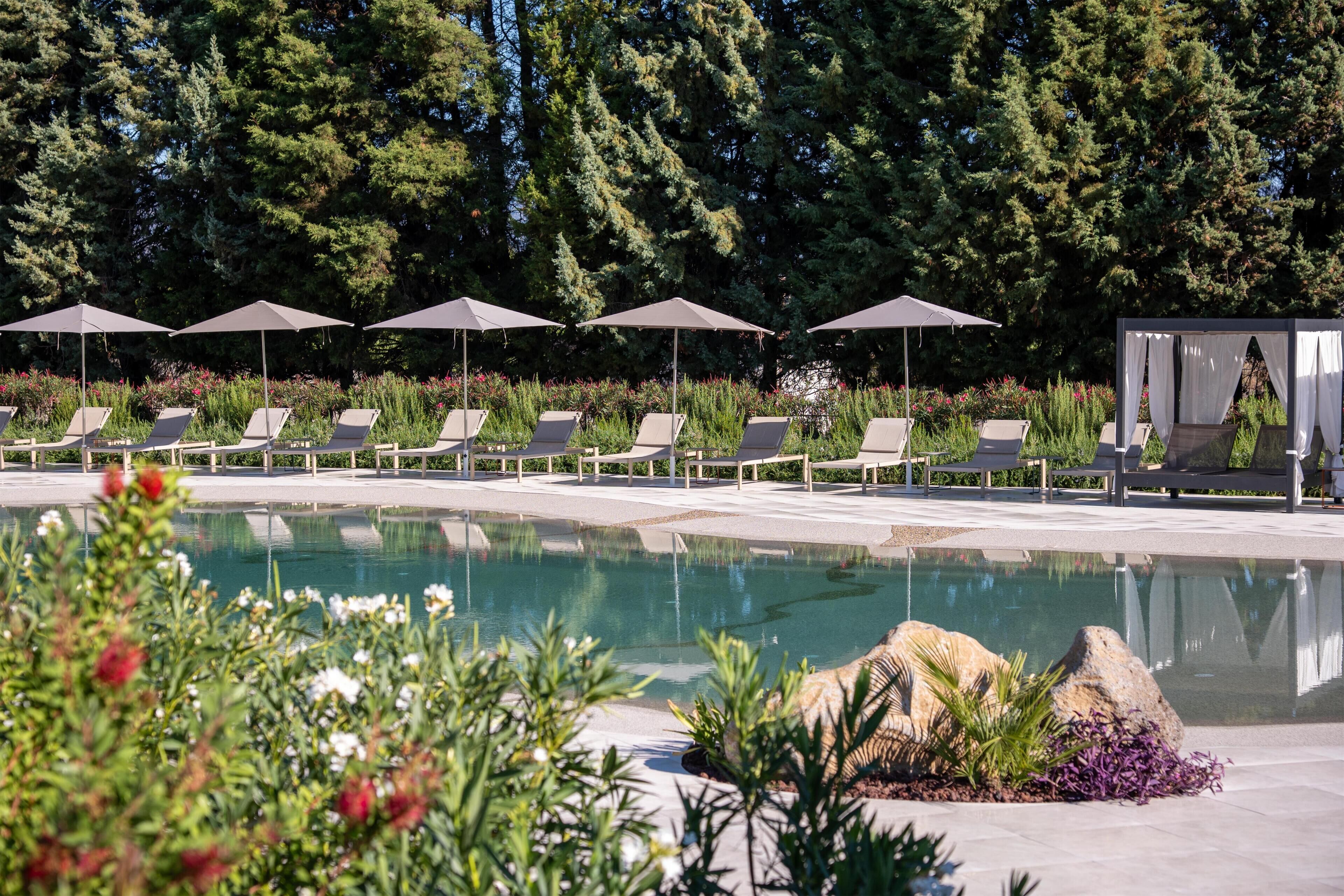 A pool area with lounge chairs and umbrellas, surrounded by greenery and trees.