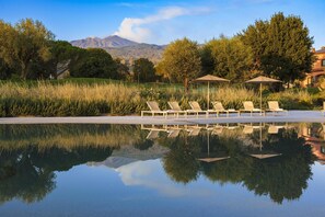A pool with lounge chairs and umbrellas, surrounded by trees and a mountain in the background. - Picciolo Etna Golf Resort & Spa, Curio Collection by Hilton (Castiglione di Sicilia)