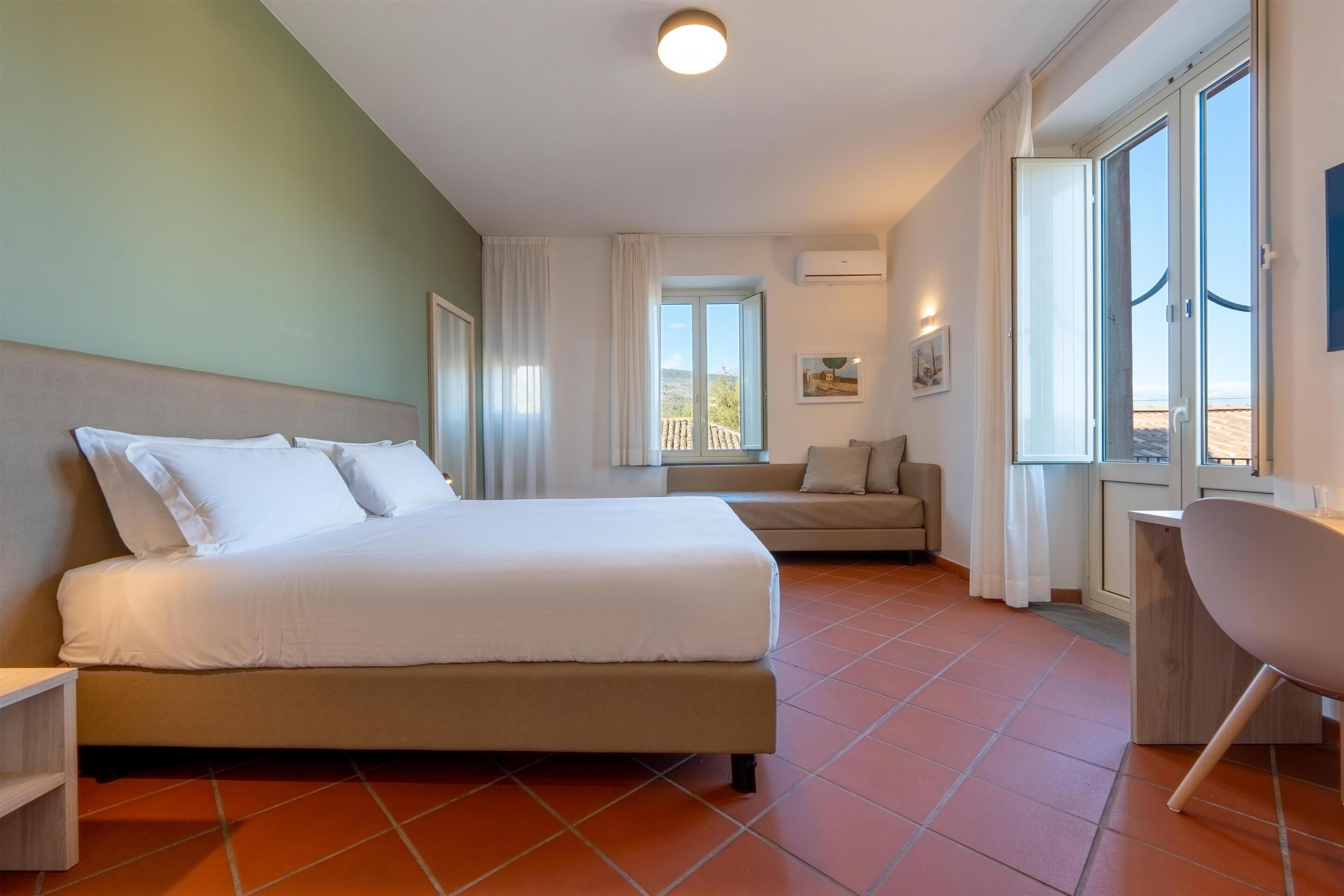 Una habitación de hotel moderna con una cama grande, un sofá, un escritorio y vistas al exterior.
