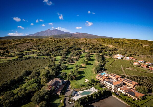 An aerial view of a golf course with a mountain in the background, surrounded by lush greenery and residential buildings. - Picciolo Etna Golf Resort & Spa, Curio Collection by Hilton (Castiglione di Sicilia)