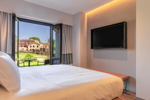 A hotel room with a large bed, a TV mounted on the wall, and a balcony with a view of buildings and greenery. - Picciolo Etna Golf Resort & Spa, Curio Collection by Hilton (Castiglione di Sicilia)
