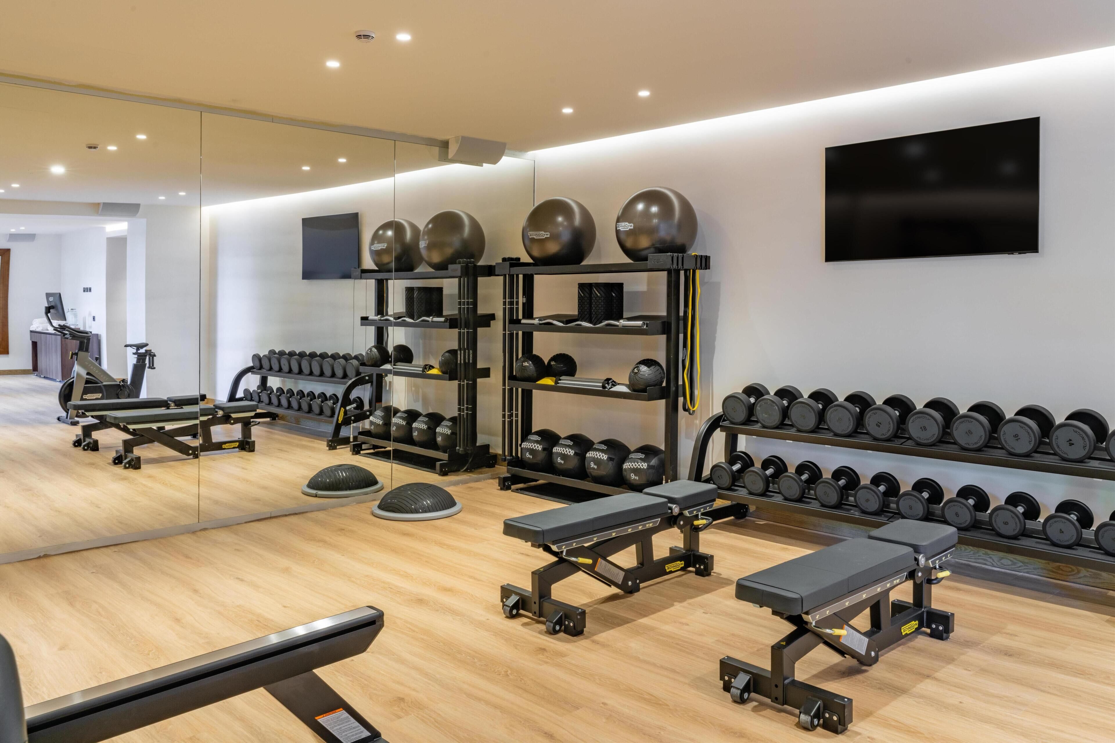 Una palestra moderna con attrezzature per esercizi, specchi e un televisore.