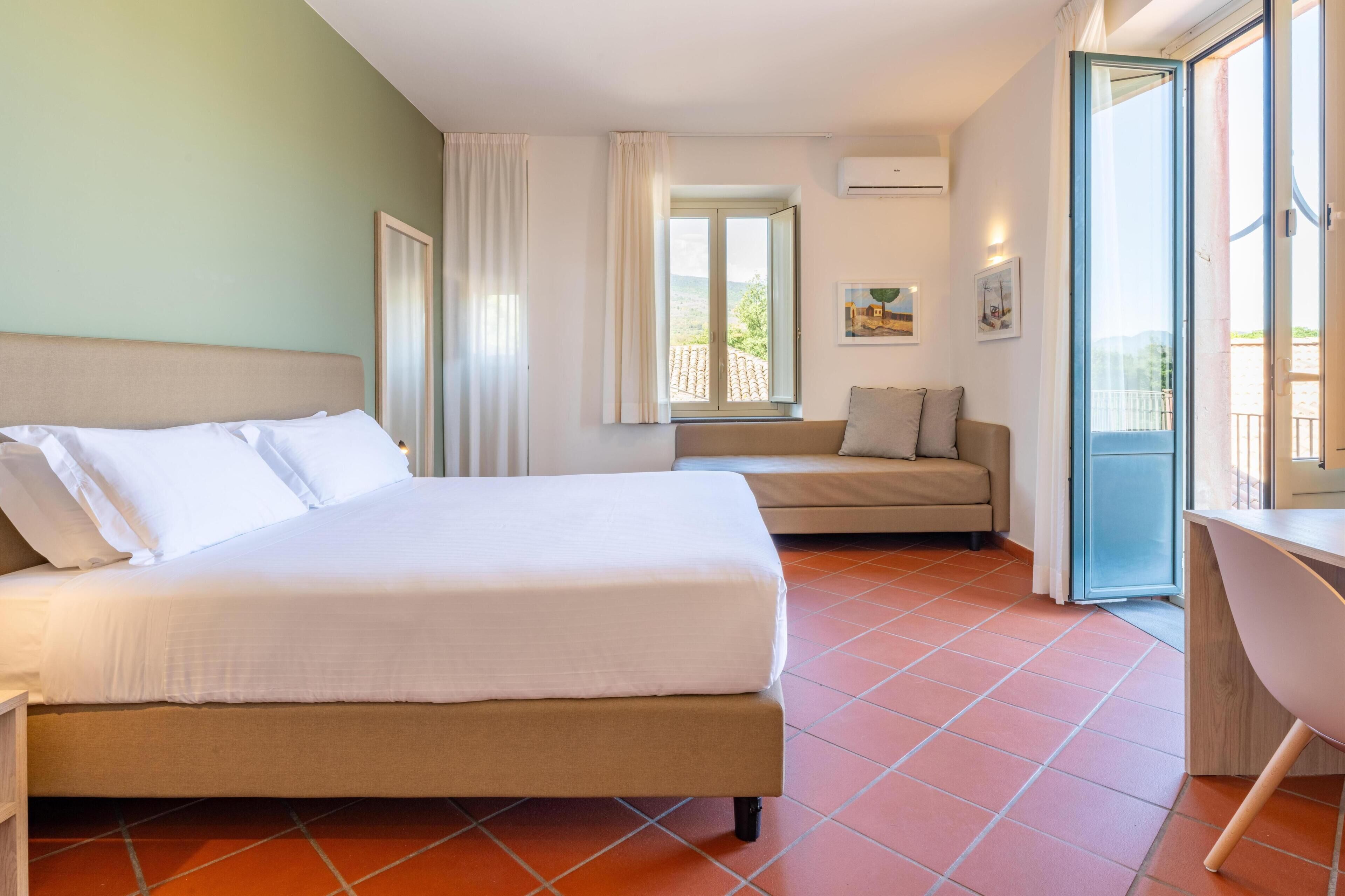 A hotel room with a bed, a sofa, a desk, and a window with a view.